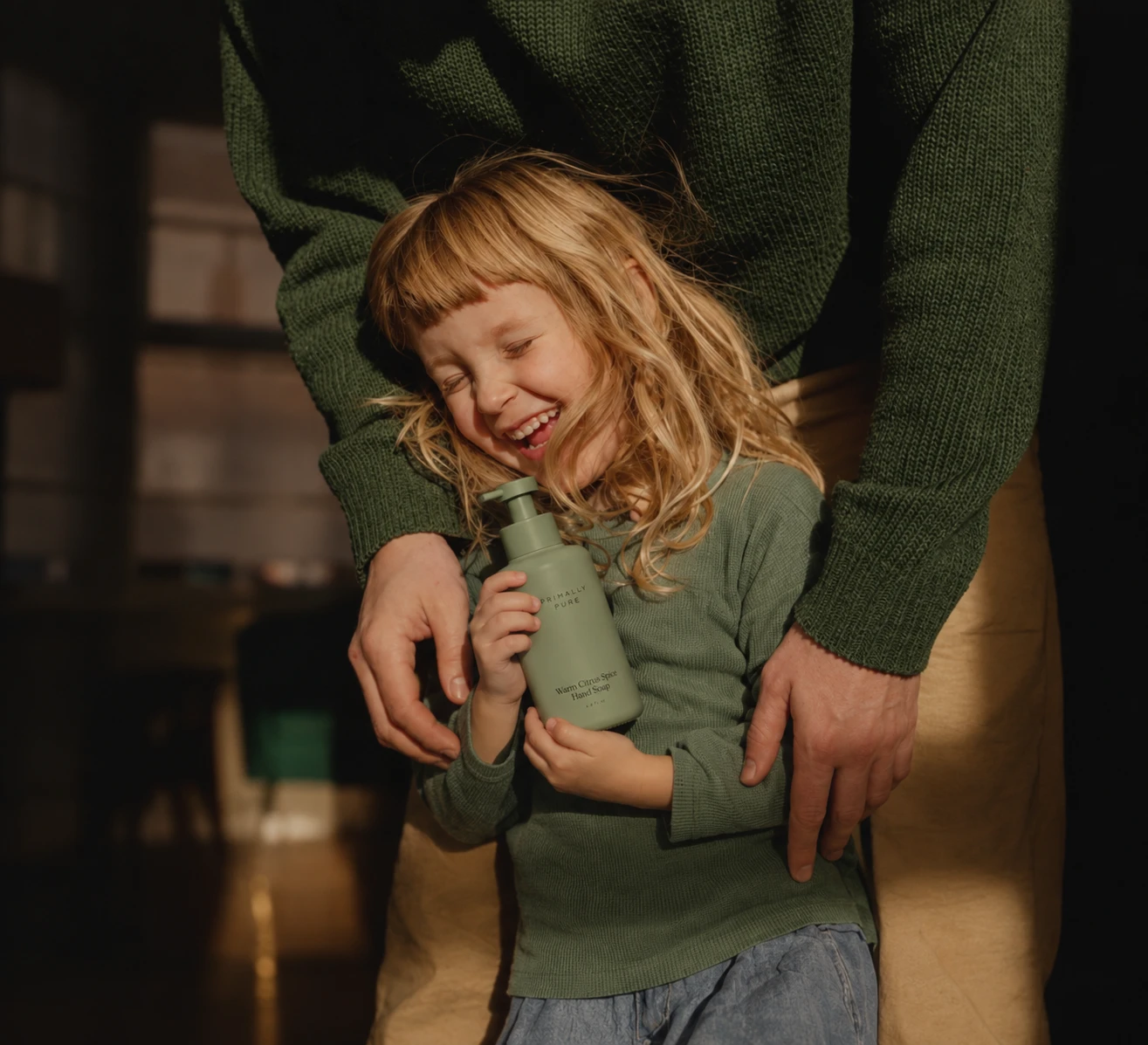 Child laughing, held by a parent, hugging a soap bottle