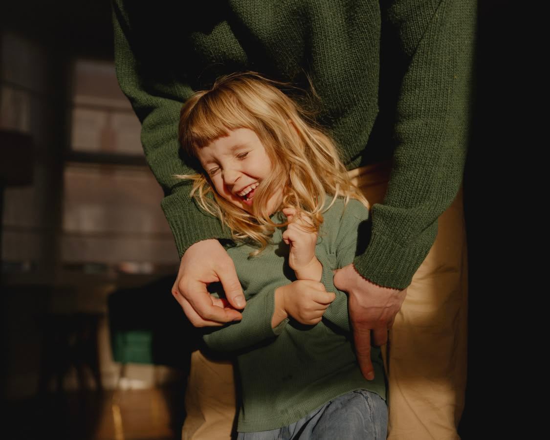 Child laughing, lifted at home in warm light